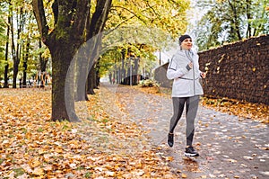 Smiling athletic woman have a jogging in the autumnal city park. Young fitness female smiling and running by the footway covered photo