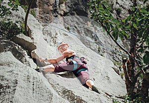 Smiling athletic woman in protective helmet climbing cliff rock wall using top rope and climbing harness in Paklenica National