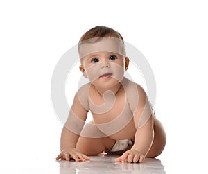 Smiling attentive infant baby toddler in diaper is crawling on all fours towards looking at camera