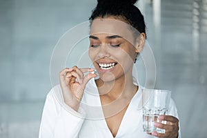 Smiling attractive african american woman taking daily dose of vitamins.