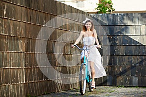 Smiling attractive girl riding blue bike down paved old city street.