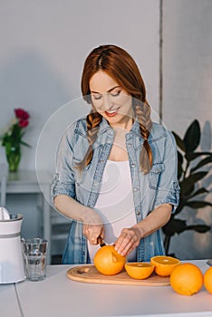 smiling attractive pregnant woman cutting oranges