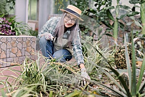 Smiling attractive retired gardener woman working in greenhouse, posing with little rake for planting flowers, looking