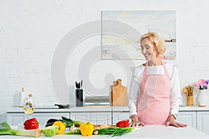 smiling attractive senior woman standing at kitchen counter and looking