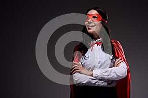 smiling attractive super businesswoman in red cape and mask standing with crossed arms