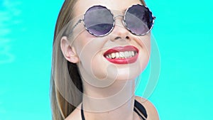 Smiling attractive woman in sunglasses seductively straightening hair in pool