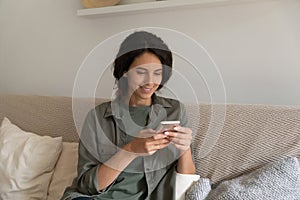 Smiling attractive woman using smartphone, relaxing sitting on couch