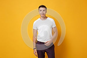 Smiling attractive young man guy 20s in white t-shirt posing isolated on yellow orange wall background studio portrait