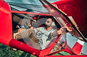 Smiling attractive young man pilot sitting in cabin preparing for take off of small aircraft