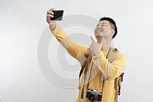 Smiling attractive young tourist with backpack walking and taking selfie mobile phone on white background. Passenger traveling on