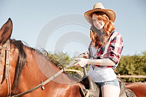 Smiling attrative young woman cowgirl riding horse