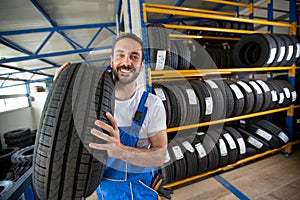 Smiling auto mechanic carrying tire