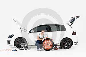 smiling auto mechanic changing car tire and looking at camera photo