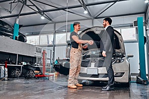 Smiling auto mechanic and client shaking hands in sevice