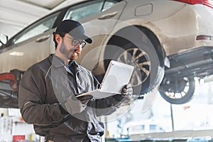 smiling auto mechanic holding a laptop and making car diagnostics in the workshop