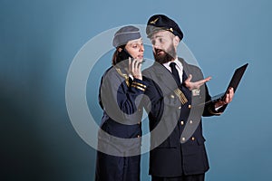 Smiling aviator using laptop while stewardess talking on smartphone