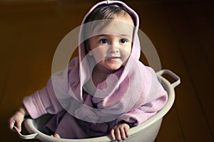 Smiling baby in a bathrobe sits in a basin