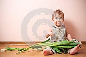 Smiling baby boy 2 years old posing with a bouquet of white tulips over pink background. Boy sitting with a flowers