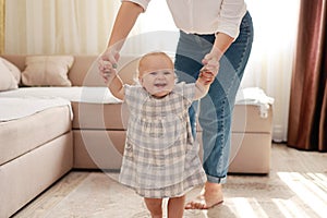 smiling baby boy girl learning to walk with mom, taking first steps with mother helping infant, teaching child at home