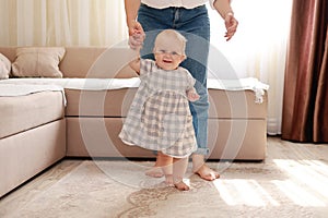 smiling baby boy girl learning to walk with mom, taking first steps with mother helping infant, teaching child at home