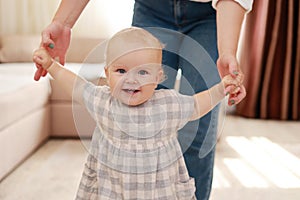 smiling baby boy girl learning to walk with mom, taking first steps with mother helping infant, teaching child at home