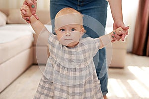 smiling baby boy girl learning to walk with mom, taking first steps with mother helping infant, teaching child at home