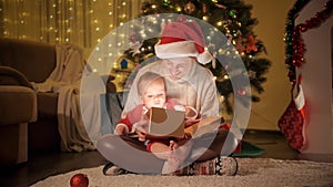 Smiling baby boy with mother opening Christmas present box and looking inside. Families and children celebrating winter