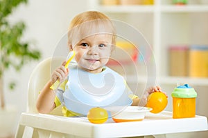 Smiling baby child boy eating itself with spoon