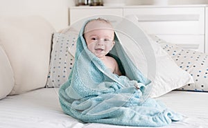 Smiling baby covered in blue towel after having bath