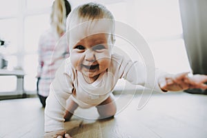 Smiling Baby Crawls and Mother Sit near Window