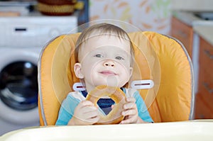 Smiling baby eating round cracknel on kitchen photo