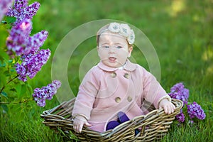 Smiling baby girl 1-2 year old wearing flower wreath, holding bouquet of lilac outdoors. Looking at camera. Summer spring time.