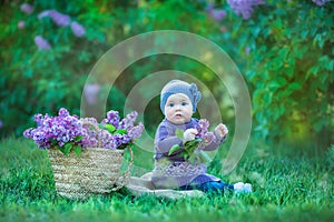 Smiling baby girl 1-2 year old wearing flower wreath, holding bouquet of lilac outdoors. Looking at camera. Summer spring time.