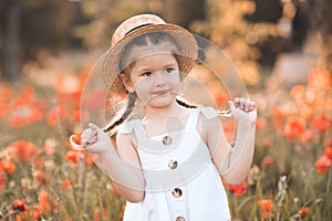 Smiling baby girl 3-4 year old wear straw hat and white rustic dress posing over nature poppy background.