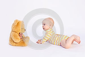 Smiling baby girl 6 months old lies on a white isolated background in a bright bodysuit in front of a soft Teddy bear, space for