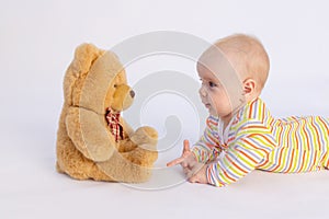 Smiling baby girl 6 months old lies on a white isolated background in a bright bodysuit in front of a soft Teddy bear, space for