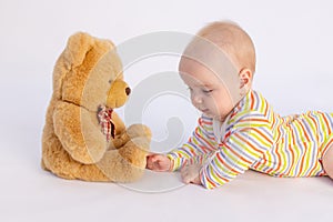 Smiling baby girl 6 months old lies on a white isolated background in a bright bodysuit in front of a soft Teddy bear, space for