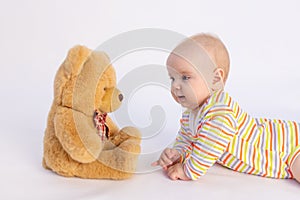 Smiling baby girl 6 months old lies on a white isolated background in a bright bodysuit in front of a soft Teddy bear, space for