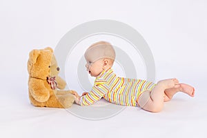 Smiling baby girl 6 months old lies on a white isolated background in a bright bodysuit in front of a soft Teddy bear, space for