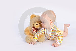 Smiling baby girl 6 months old lies on a white isolated background in a bright bodysuit with a soft Teddy bear, space for text