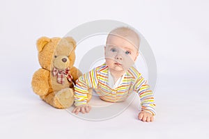 Smiling baby girl 6 months old lies on a white isolated background in a bright bodysuit with a soft Teddy bear, space for text