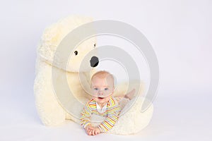 Smiling baby girl 6 months old lies on a white isolated background with a large soft Teddy bear, space for text