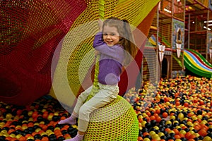 Smiling baby girl swinging on hanging ball playing in balls pool