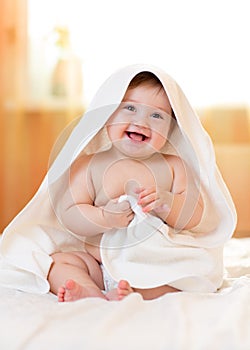 Smiling baby girl under towel after bathing