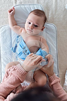 Smiling baby is having fun with her mother while changing his diaper at home