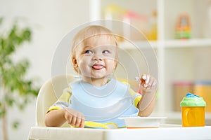 Smiling baby kid boy eating itself with spoon