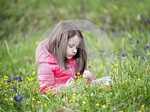 Smiling baby with long dark hair. Cute little girl is sitting in the woods on a grass and enjoying