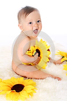 Smiling baby sitting on the fur in a full-length with sunflowers in his hands