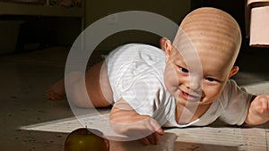 Smiling baby trying to catch an apple on the floor