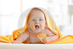 Smiling baby under soft towel. Cute child lying on bed after bathing in living room